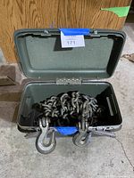 Open green metal storage box containing heavy-duty galvanized chain with two clevis grab hooks hanging out from the front of the box.