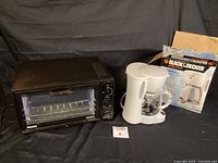 Kenmore black toaster oven with glass door, wire rack inside and three control dials on the right, shown alongside white Black & Decker 6-cup coffee maker with original box.