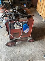 Front angle of red Lincoln AC-225-S arc welder on cart with cables and electrode holder coiled on top