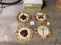 Four round mosaic stepping stones arranged on concrete floor with box in background. Each stone depicts a different animal - turtle, dragonfly, butterfly, ladybug.