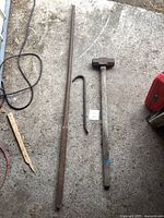 Photo showing two metal pry bars and one sledgehammer laid flat on concrete floor, with visible rust and wear.