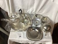Overall view of silver tea set pieces including teapot, creamer, sugar bowl, trays and caviar butter dish.