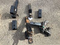 Photo showing various trailer hitch ball mounts and hitch receivers on asphalt surface, with some rust and wear visible on items.