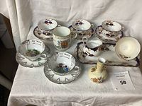 Full view of the entire lot including all china pieces arranged on white cloth background showing various cups, saucers, mug, miniature vase, and tray.