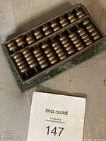 Medium size Chinese soroban abacus with brass beads on metal rods in a brass frame resting on a green marble base.