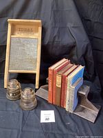 Photo showing all lot items: wooden IDEAL washboard, two glass insulators, seven vintage hardcover books in assorted colors, and two railroad track bookends holding books.