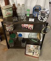 Full view of vintage jars, bottles, eye wash cup, tin cans, and collectible tins arranged on a wooden shelf