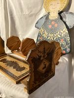 Photo shows foldable adjustable wooden book stand decorated with silhouette art, three octagonal wooden bookends, and folk art wooden angel decoration in background.