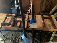 Woodworking clamps laid on a wooden board showing 5 C-clamps and 2 pipe clamps, highlighting condition and paint.