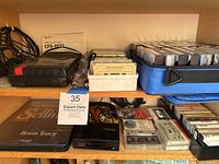 Shelf with Realistic portable cassette player, numerous cassette tapes in cases and boxes, some cables and other audio accessories