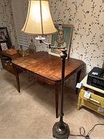 Full view of the lit floor lamp standing next to a wooden table and chair in a room with floral wallpaper.