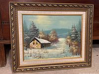 Framed winter cabin oil painting showing complete work and frame.