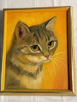 Full view of the framed cat painting with a yellow-orange background, showing the cat's face and signature at the bottom left corner.