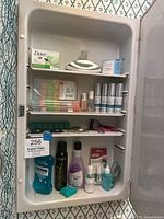 Medicine cabinet with three shelves containing various health and beauty items shown from a distance.