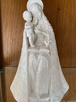 Front view of white porcelain Virgin Mary holding child Jesus figurine with floral cloak details.
