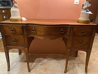 Front view of vintage wooden sideboard with five drawers and brass handles, showing curved design and wood inlay decoration.