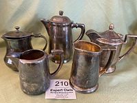 Group photo showing five vintage silver-plated teapots and pitchers with varied sizes and patina.