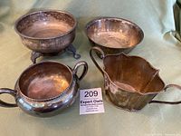 Four silverplate bowls displayed on a cloth surface showing tarnish and different bowl styles