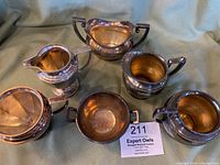Seven silverplate items displayed together on a cloth, including sugar bowls and creamers of various sizes and shapes.