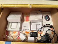 First photo showing both pairs of wireless headphones in their boxes, several chargers and cords, and a smart bracelet box with manual.