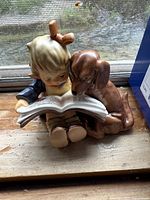 Front view of Hummel figurine depicting blond boy reading a book with brown dog seated beside him.
