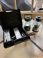 Overview showing camping stove, two lanterns, and a pocket knife box on table