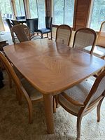 Dining table with eight chairs around it, showing wood grain pattern and chairs with caned backs and fabric seats.