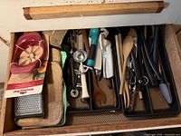 Full drawer showing assorted cooking tools and pot holders organized in black plastic tray inserts.