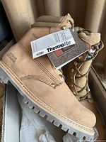 Side angle view showing new tan leather boot with attached tags indicating Thermolite insulation.