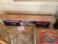 Boxed foldable hammock with canopy, placed on carpet floor along with furniture