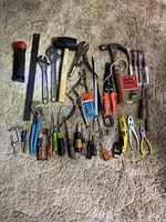 Photo shows all tools laid out on carpet including wrenches, mallet, hammers, pliers, screwdrivers, flashlight, clamps, and hardware items.