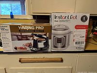 Waring Pro Belgian waffle maker box next to Instant Pot Duo box on a kitchen counter.