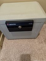 Front view of the Sentry 1170 safe showing the black locking panel with keyhole and brand label, positioned on carpeted floor.