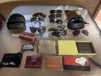 Photo showing sunglasses and wallets on a glass table with multiple items including sunglasses in cases and wallets.