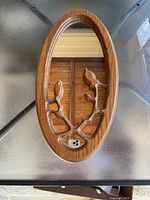 Full view of oval wooden framed mirror with floral cutout design in the lower part of the frame