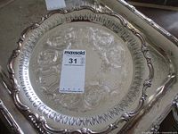 Full view of round silverplated tray showing ornate pierced edge and central engraved decorations with inventory tag on top.