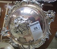 Top view of the ornate silverplate lid showing detailed floral design and handle, with sticker.
