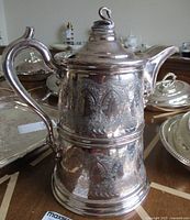 Full view of antique Reed & Barton engraved silver-plated double wall water pitcher with ornate patterns on body, curved spout, and leaf branch handle.