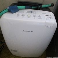 White Garrison dehumidifier showing front view with control buttons and attached green hose.
