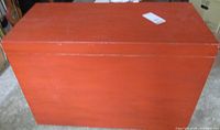 Overall view of the rectangular orange painted trunk with smooth flat top and no visible hardware on top surface.