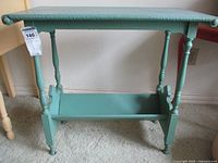 Front view of green painted vintage side table with carved top edge and four legs with bookshelf below.