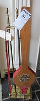 Photo of the brass fireplace tool stand with three brass tools visible and wooden bellows hanging on the stand. The bellows feature red leather sides and a brass emblem.