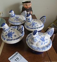 Four cobalt blue and white Hen on Nest casserole dishes arranged on a table with a Hummel monk pitcher behind them.
