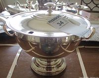Front view of large silverplate pedestal soup tureen with lid and side handles, tag visible.