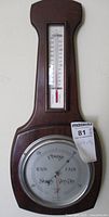 Full view of the wooden barometer mounted on a wall showing the thermometer above and barometer dial below.