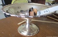Side view of the raised silver compote with two silver wine spouts resting inside, one spout having an additional small cork stopper.