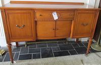 Front view of vintage solid wood buffet showing doors, drawers, carved details, and turned legs.