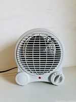 Front view of the small white desk fan heater showing circular grill, power button, and rotary heat control dial with red indicator light.