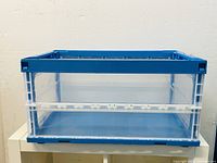 Side view of the foldable storage container showing the clear plastic sides with blue frame