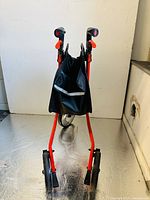 Front view of the foldable red three-wheel walker showing the walker folded with storage bag attached.